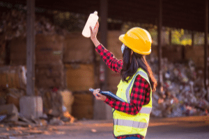 Female worker wearing hard hat and hi-vis vest, analysing waste on a work site.
